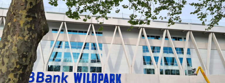 Blog 17 BBBank Wildpark Schriftzug an der Stadionfront mit Baustellenfahrzeugen und Bauzaun im Vordergrund