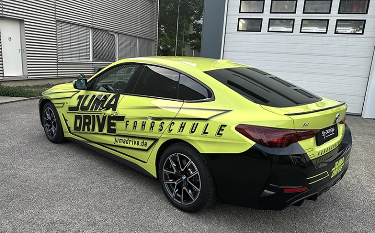 Neongelber BMW i4 mit Juma Drive Fahrschule Beklebung und schwarzem Heck.