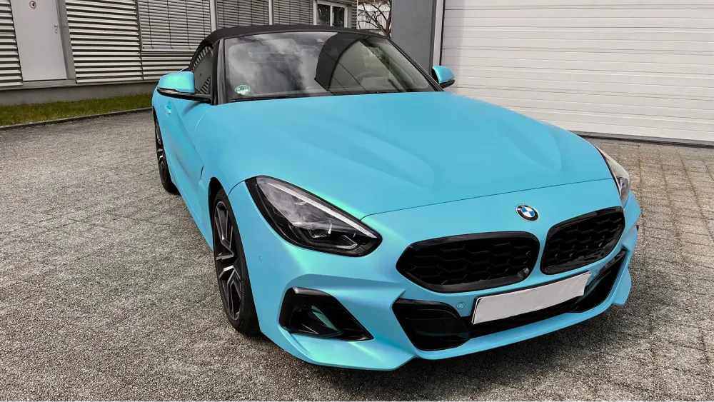 BMW Z4 Cabriolet in mattem Hellblau mit schwarzem Verdeck vor einer Werkstatt.